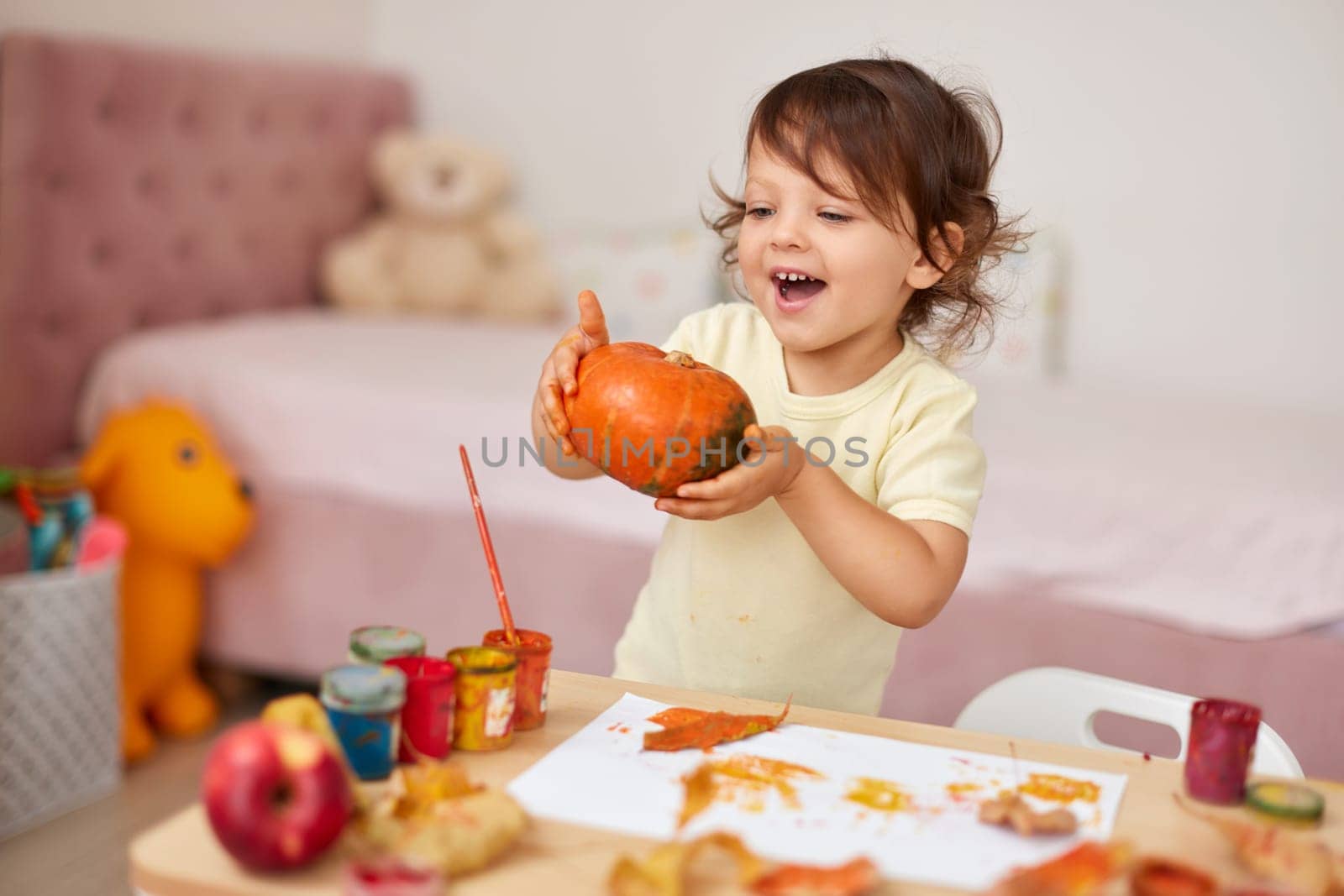 happy little child girl painting Halloween pumpkin. smiling baby girl drawing autumn pumpkin in yellow paint
