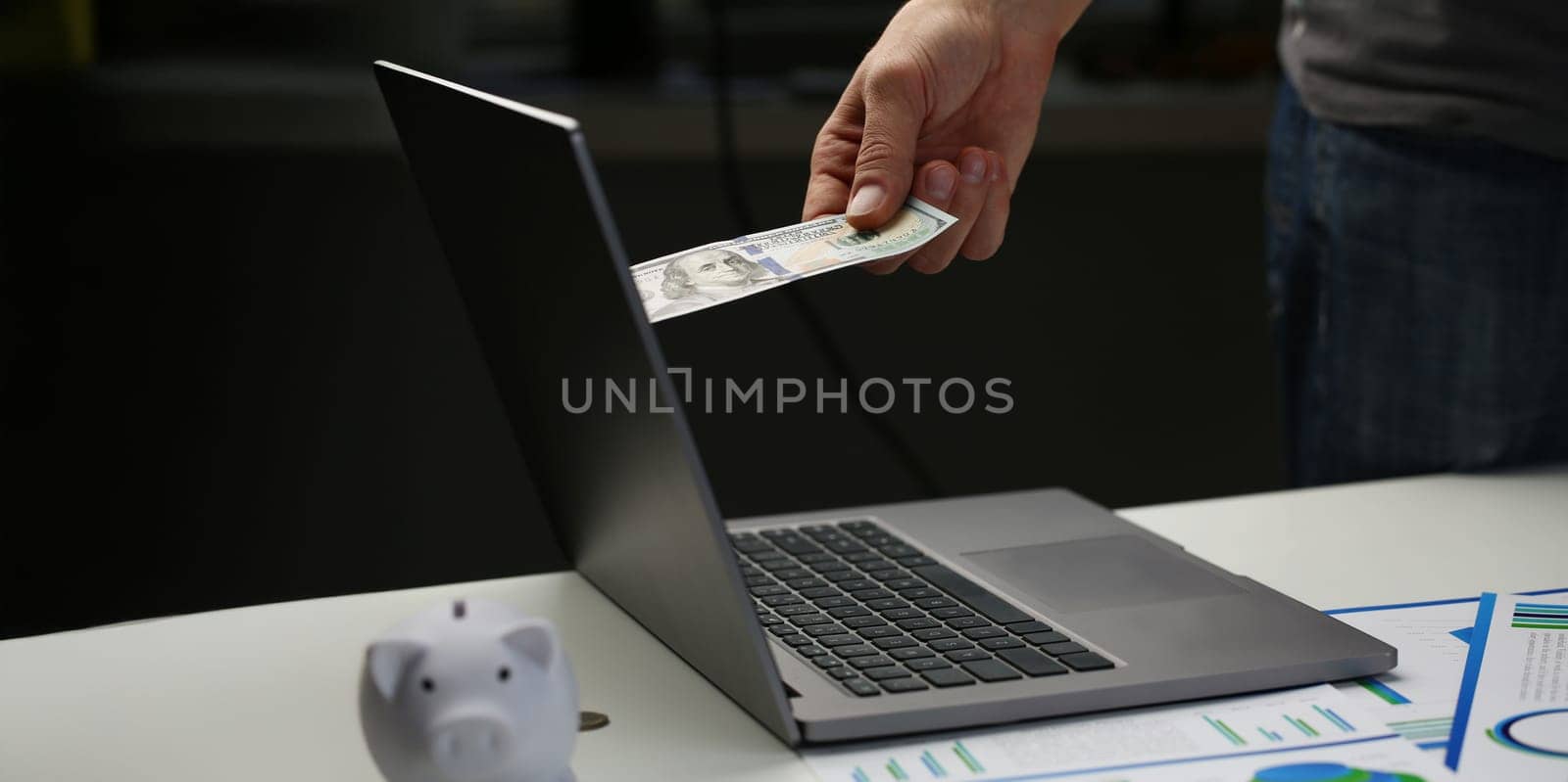 Close-up of man invest money through computer screen, put banknote to online bank. Guy pay online for purchase, fast transaction. Online operation concept