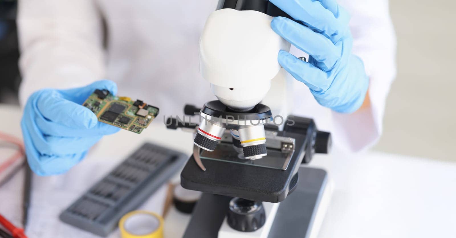 Close-up of person put smartphone component under microscope for investigation. Man wants to see tiny details on board. Tech, repair service, lab concept