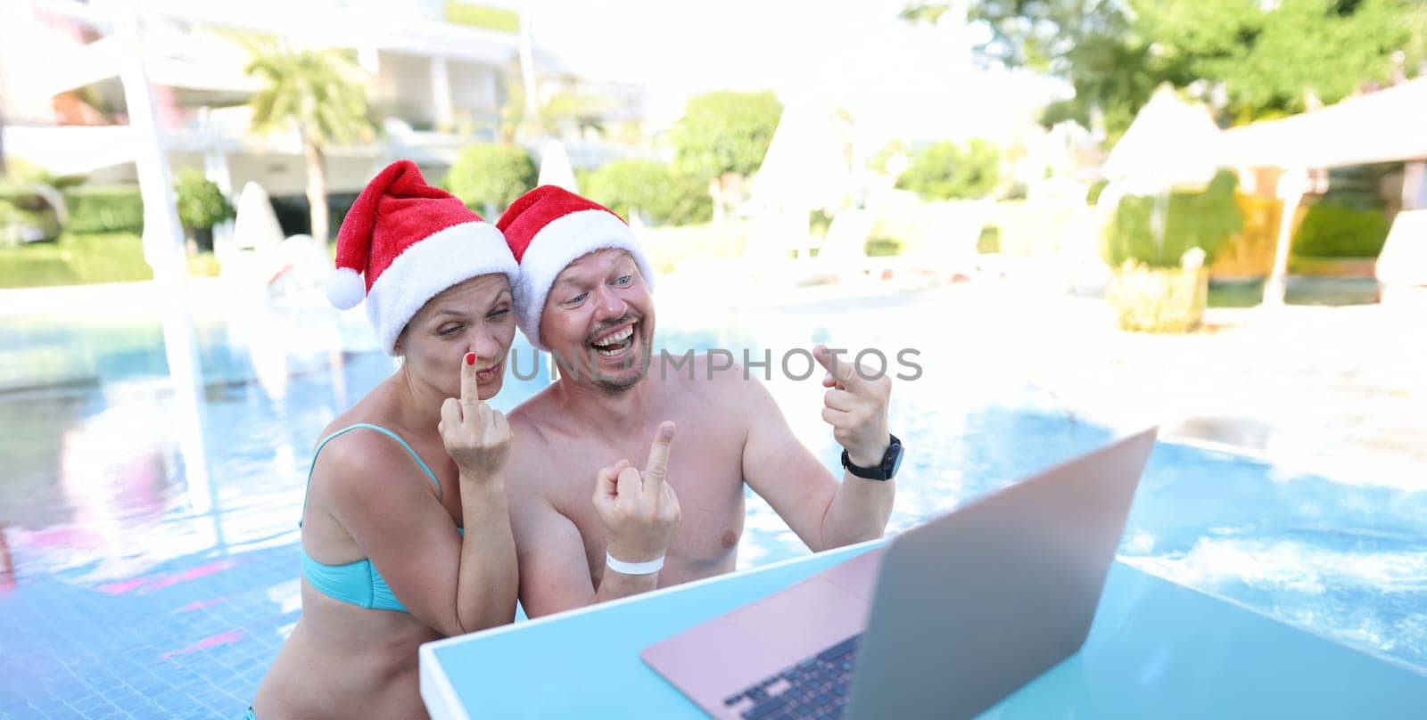 Man and woman in santa claus hats show fucking gesture into monitor. Remote work and rest in quarantine concept