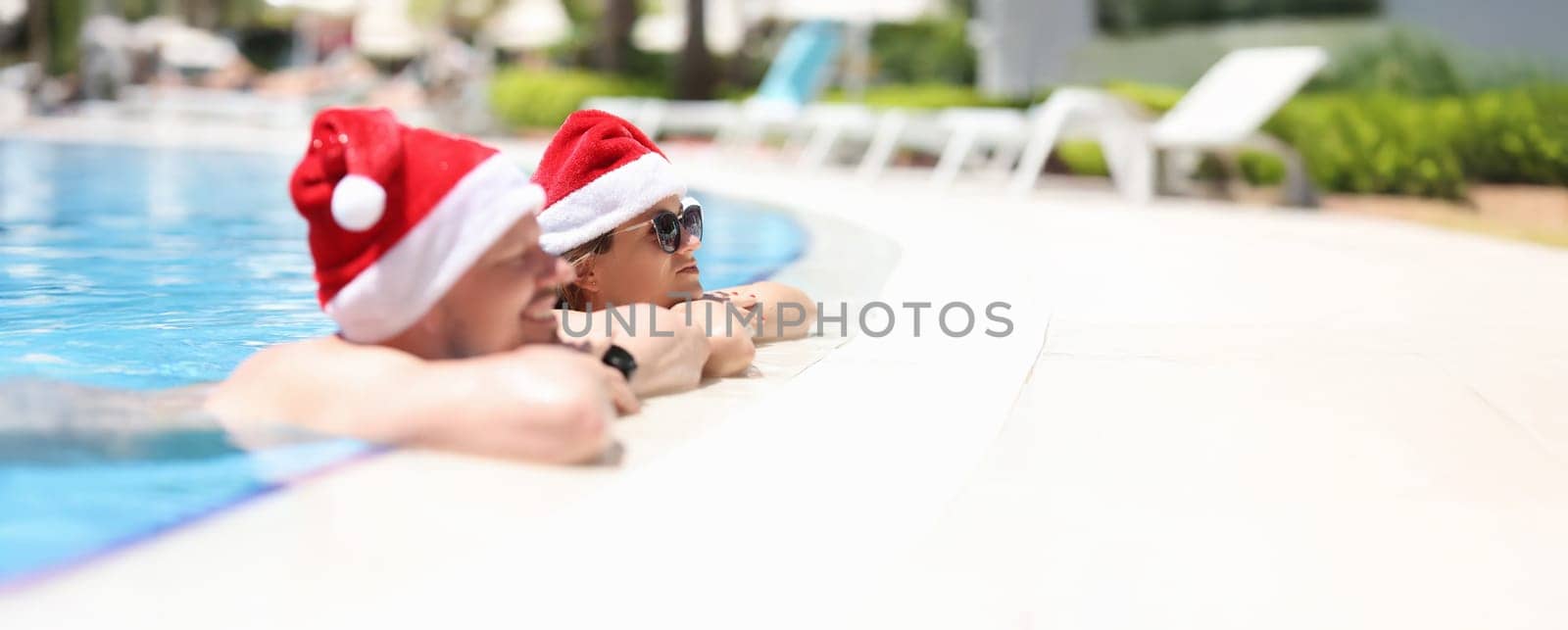 A man and women in santaclaus hats are resting in the pool, close-up. New Year in hot countries at the resort, december