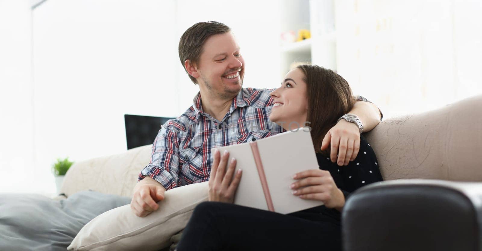 Portrait of middle aged father and young daughter reading book together sitting on couch at home. Happy emotion and quality time together. Family concept