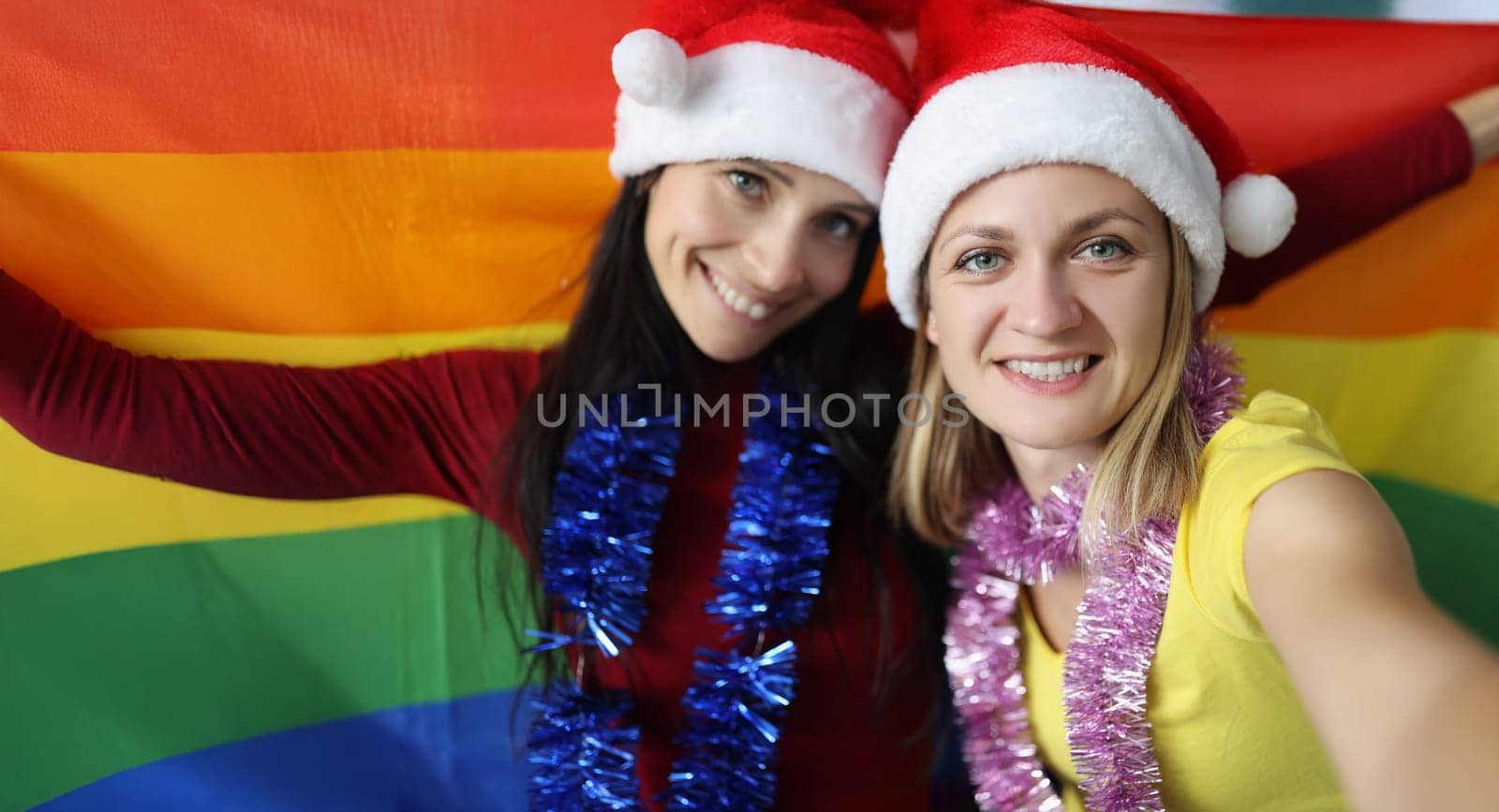 Portrait of female lovers happy about new year celebration hold lgbt flag. Smiling couple posing for picture. New year party, christmas, holiday concept