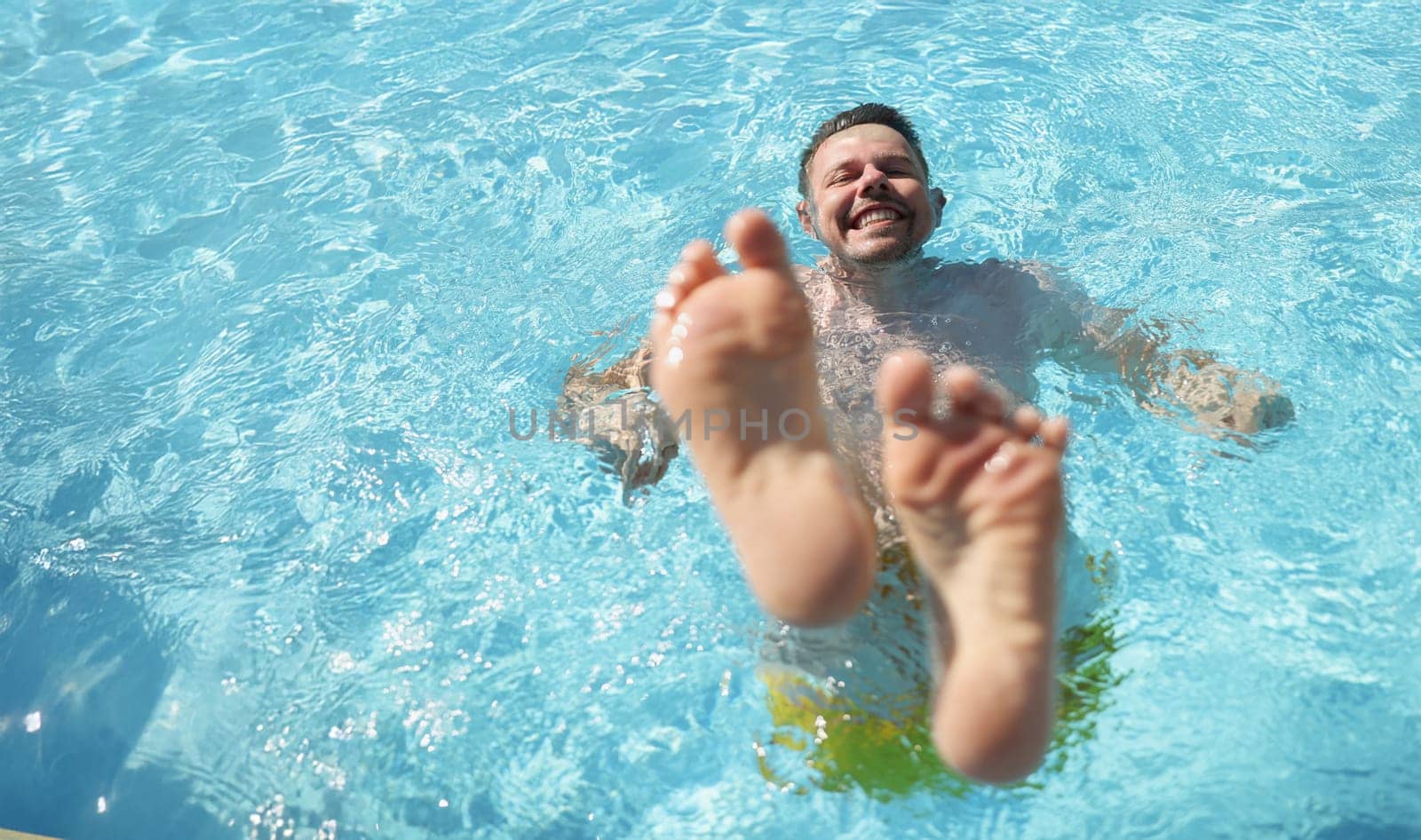 Portrait of man diving into water in swimming pool with feet up. Laughing cheerful middle aged male enjoy summer hot water. Summertime, fun, chill concept