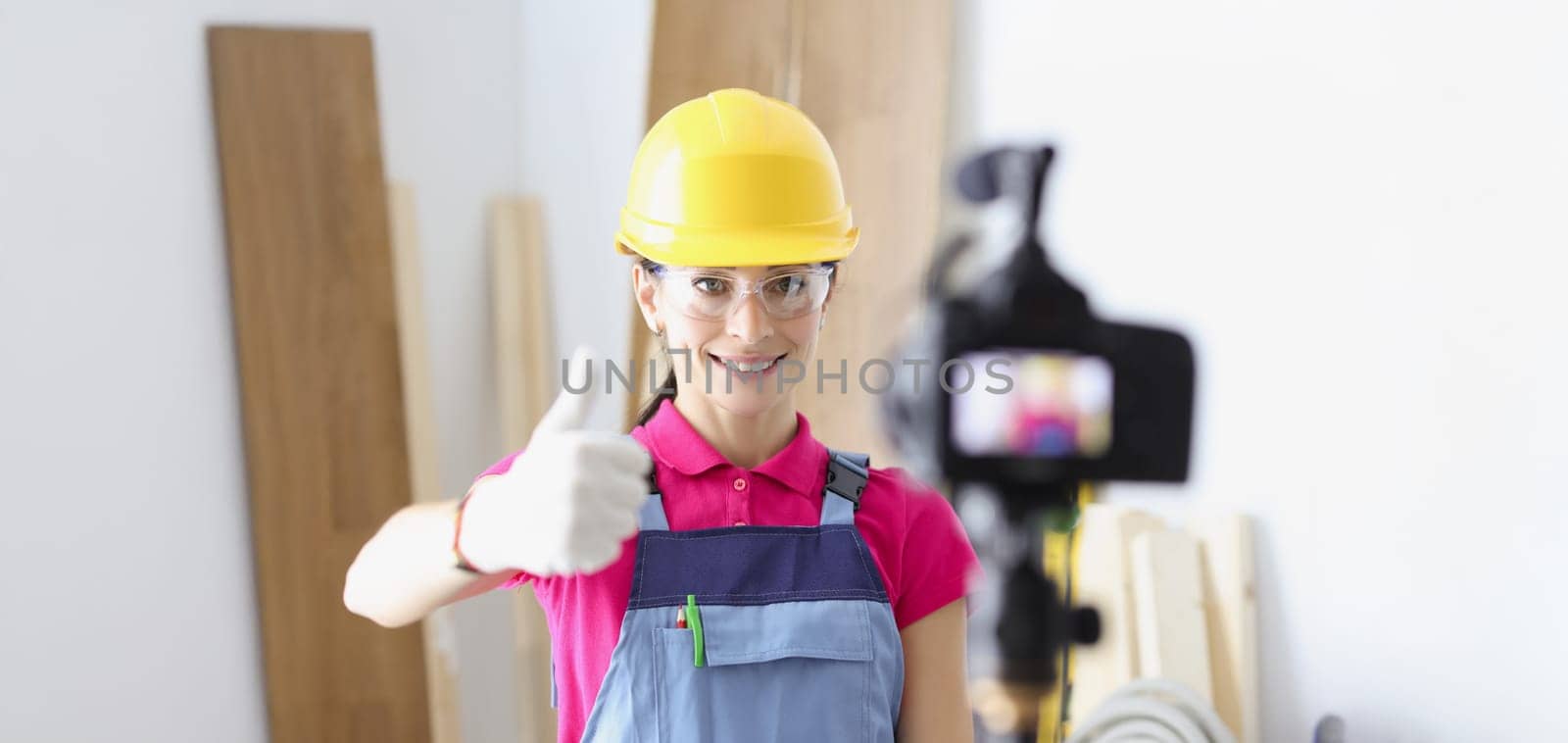 Portrait of happy woman construction site worker show thumbs up on camera. Film process on camera as educational lesson. Renovation, design, tech concept