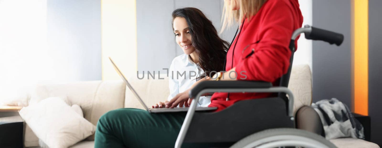 Portrait of best friends spend time together watching movie on laptop, woman in wheelchair hold device on lap. Disabled people, sisterhood, pastime concept