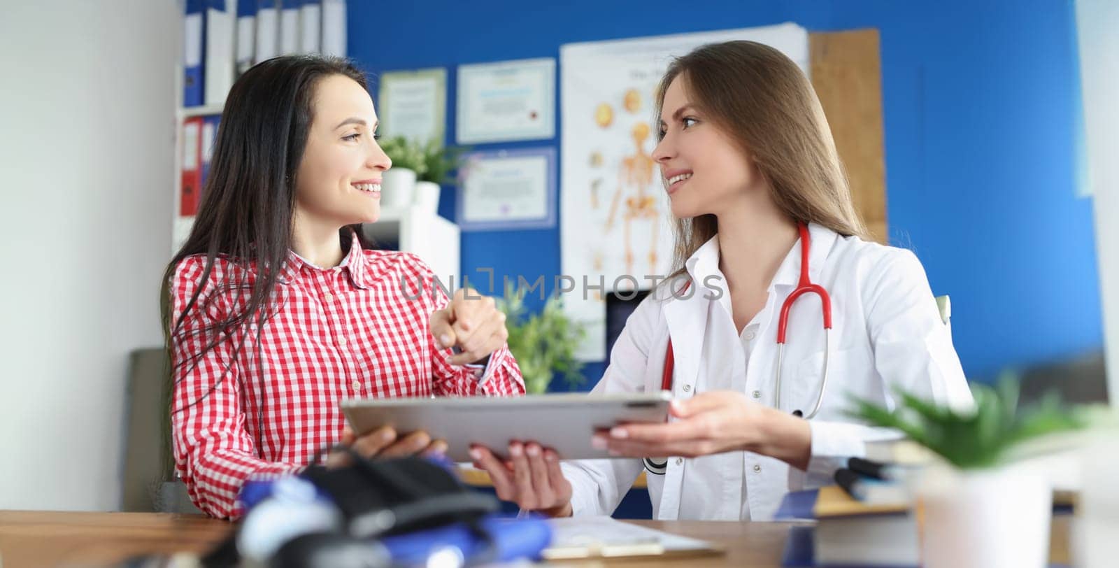 Portrait of patient and family doctor talking about health checkup, sign prescription on tablet. Smiling client and doctor in clinic. Appointment concept