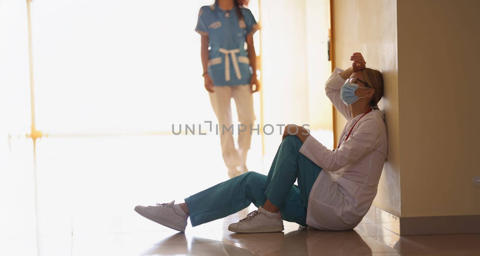 Low angle of exhausted surgeon after long operation sitting in hospital corridor. Bad news, rest after hard operation. Medicine, save life, health concept