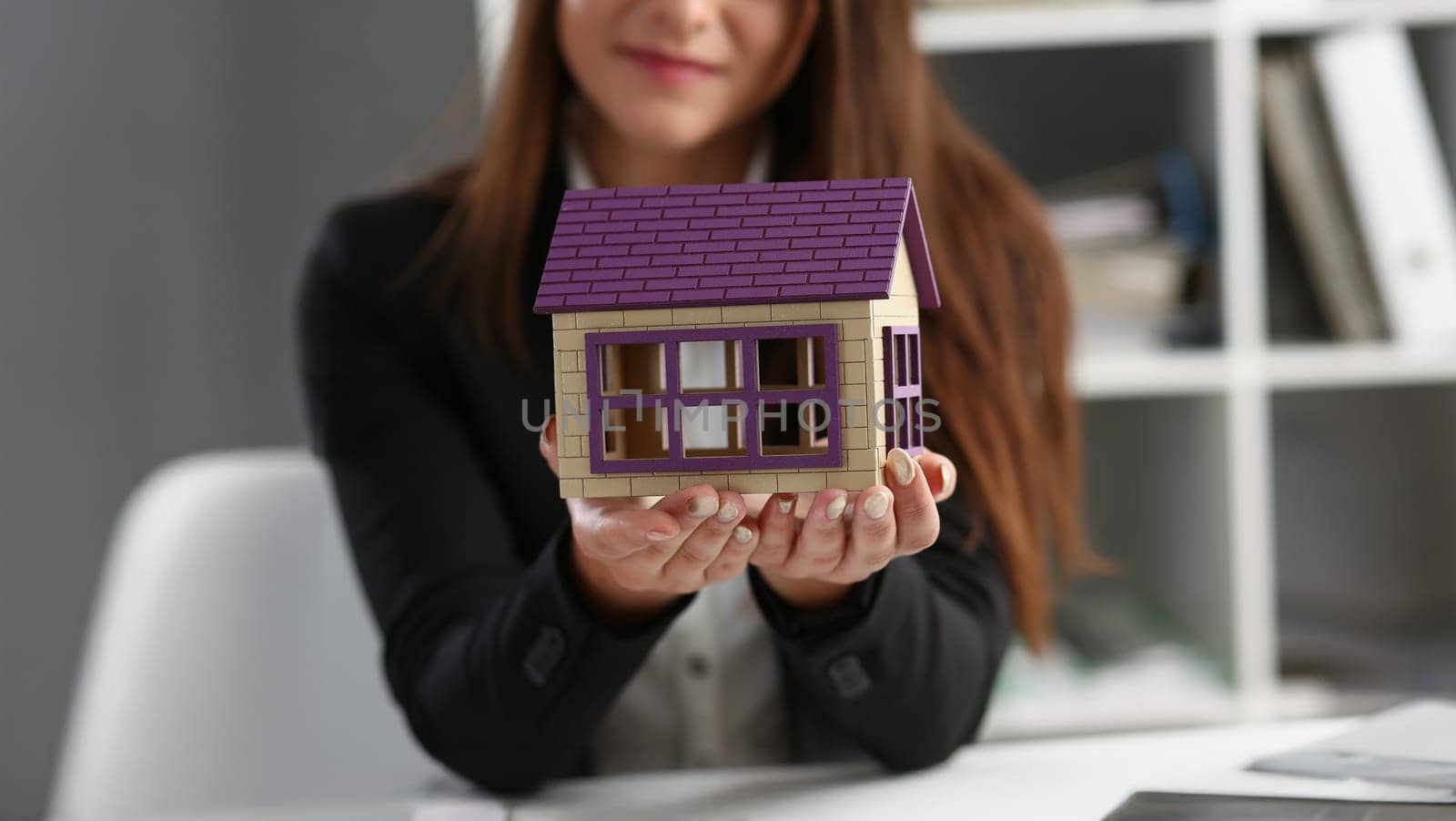 Close-up of woman in office hold miniature toy house in hand symbol of real estate. Sale or rent construction of apartment and housing for families concept