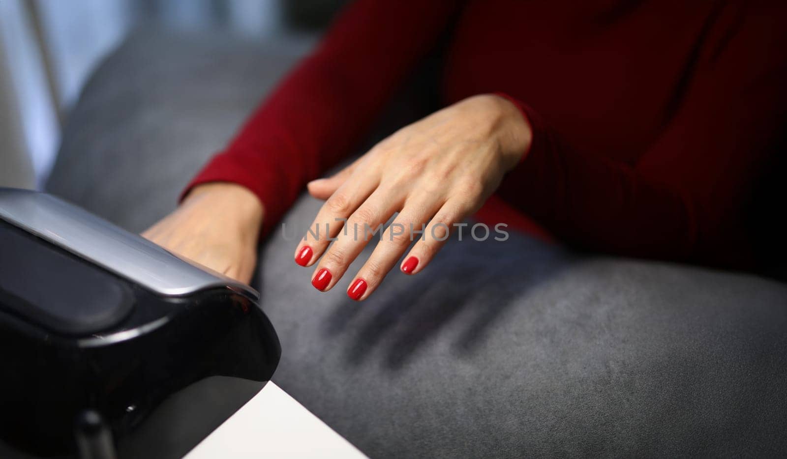 Close-up of woman client putting hand with fresh red nails under lamp to dry it. Spend time on beauty procedure in luxury studio. Beauty, wellness concept