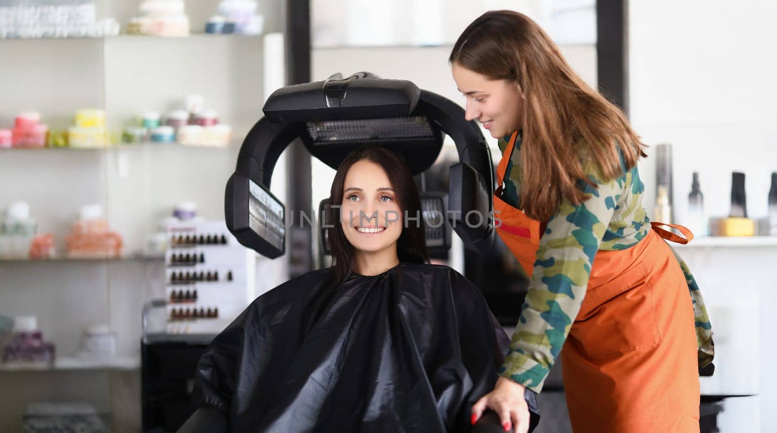 Portrait of young lady under hairdressing machine while looking in mirror. Visit master for beautiful look and good hair quality. Self care, beauty concept