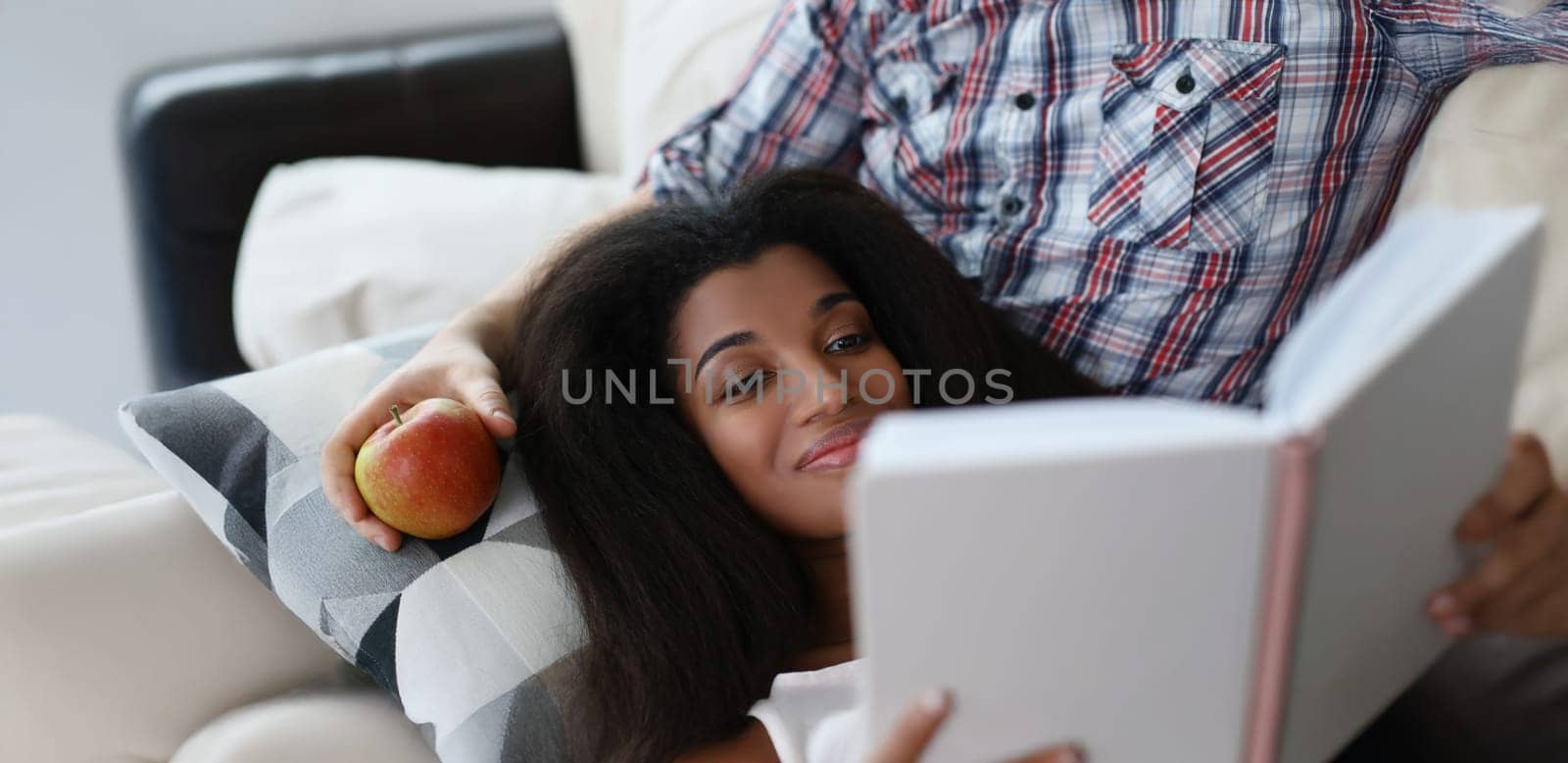 Portrait of latino american young woman reading interesting book laying on fathers lap. Smiling female get new knowledge, spare time at home. Hobby concept