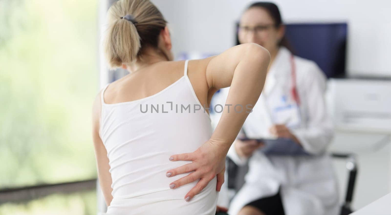 Close-up of female patient complain on back pain and touch side of body. Doctor listen to client and propose diagnostic. Healthcare, trauma surgeon concept