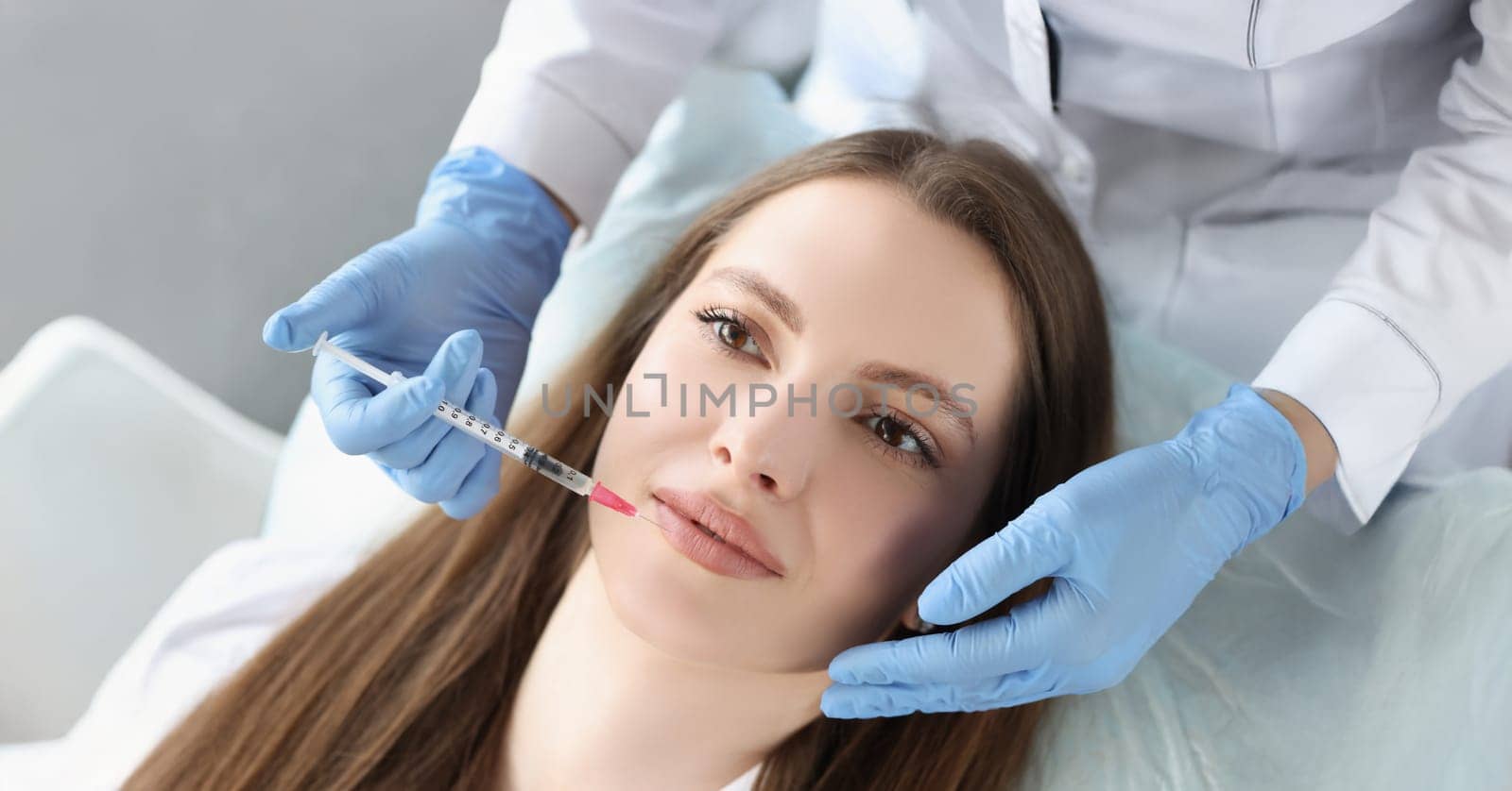 Portrait of young woman gets injection of botox in her lips, cosmetologist using syringe. Cosmetology, beauty treatment, plastic surgery, clinic concept