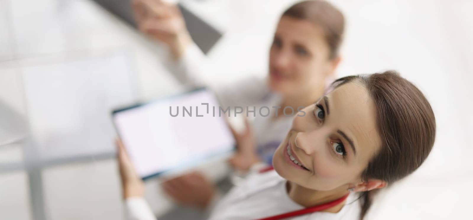 Top view of women working in hospital spend pause with tablet device. Smiling nurse hold gadget with white screen. Pause from work, pastime, clinic concept