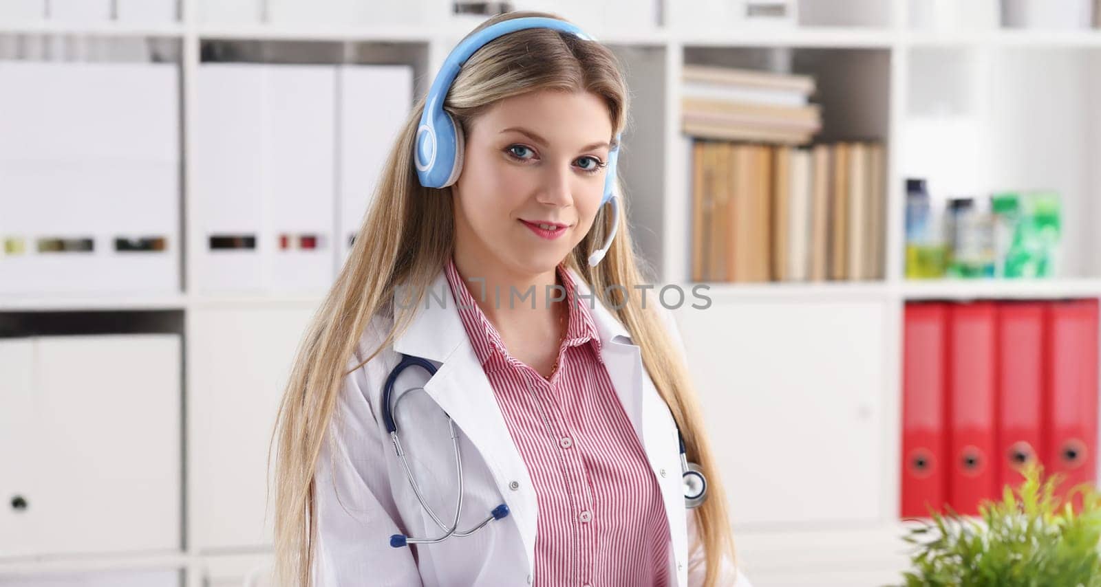 Portrait of pretty female blonde doctor talking to patient over wireless headset advises medical problem. Remote education, internship, callcenter concept