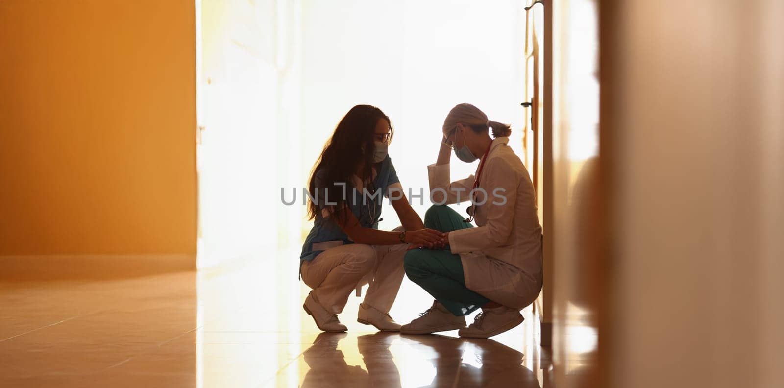 Low angle of tired medical worker after hard long surgery sitting on floor. Nurse support colleague doctor. Medicine, save life, health, tragedy concept