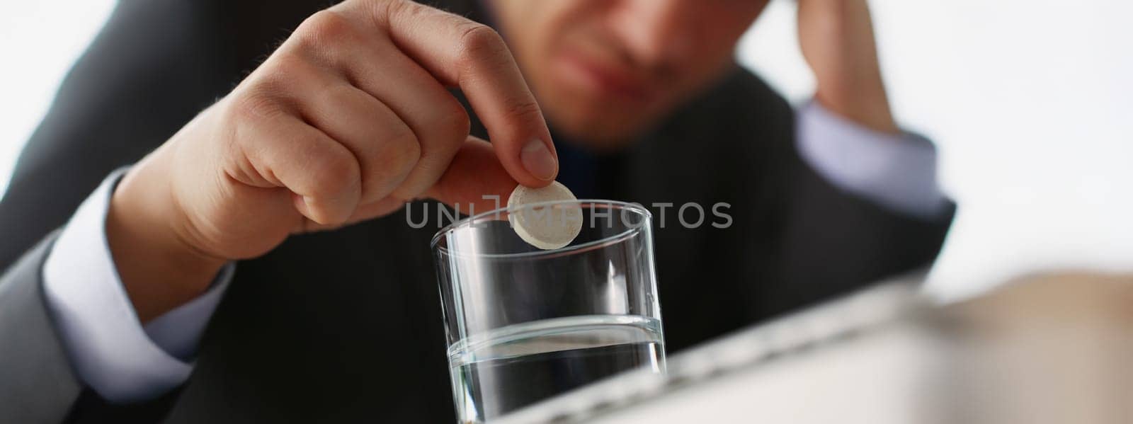 Close-up of tired man put tablet in glass with water to stop headache because of big workload. Aspirin medication to relief pain. Medicine, remedy concept