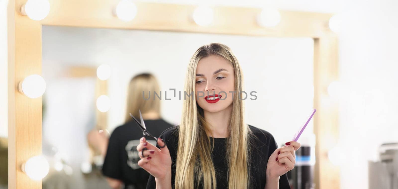 Portrait of young lovely professional master holding tools for work and posing. Qualified hairdresser hold scissors and comb. Beauty studio, barber concept