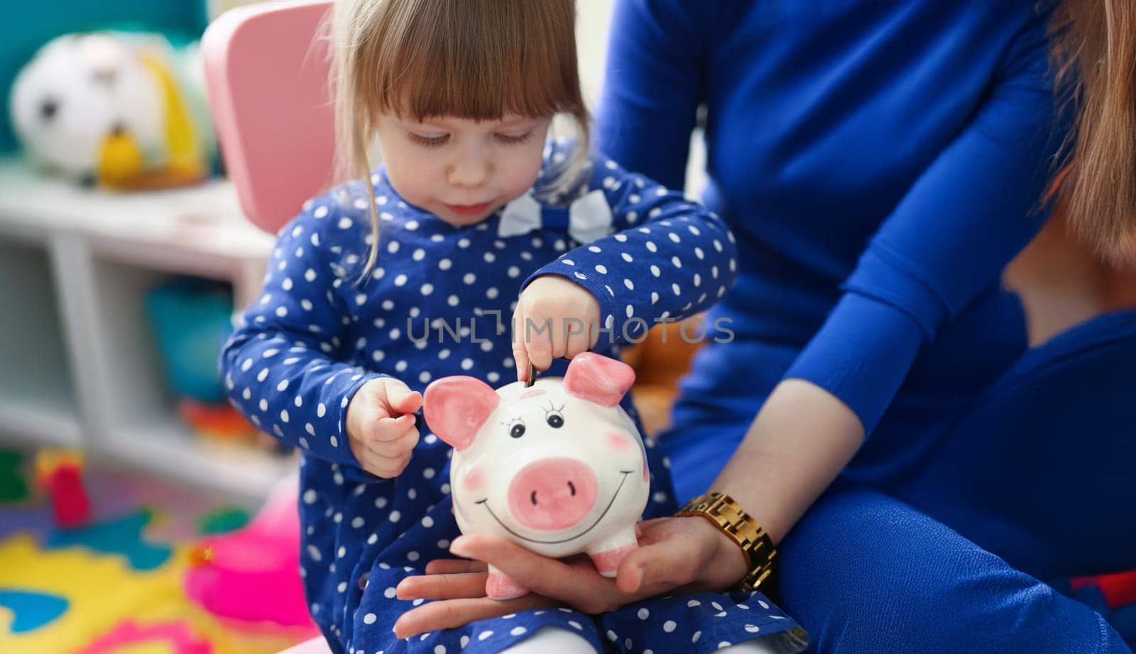 Portrait of cute little child putting coin cash into piggy bank container. Mother teach daughter to save up, save to buy toy. Childhood, investment concept