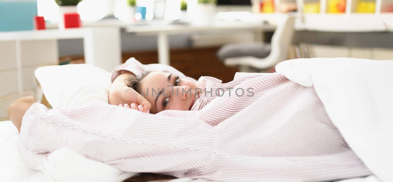 Portrait of happy young woman waking up in cozy home bed in good mood. Lovely female in pyjamas stretching after waking up. Good morning, awake concept