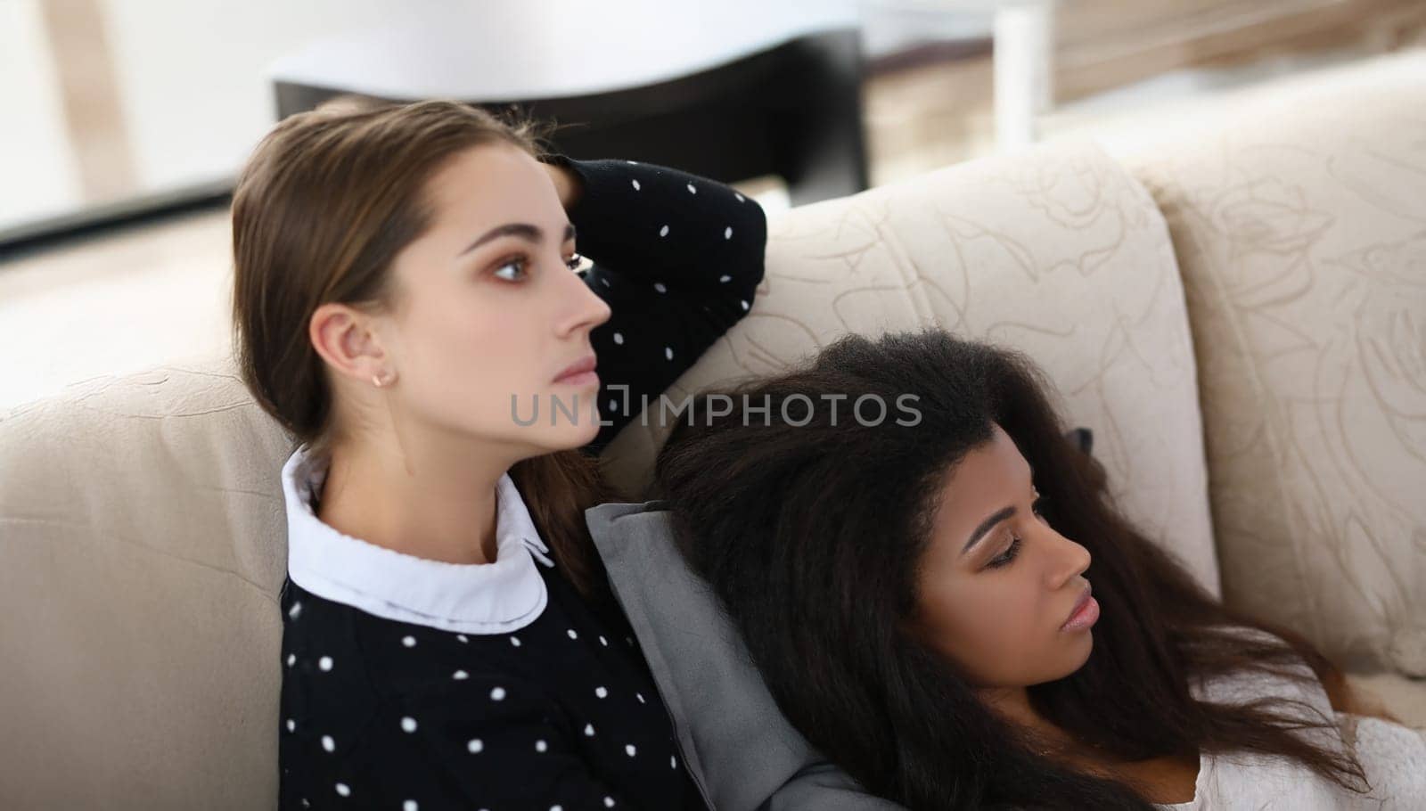 Portrait of brunette woman and her latino american friend watch television at home on couch. Concentrated friends listen news. Leisure, friendship concept