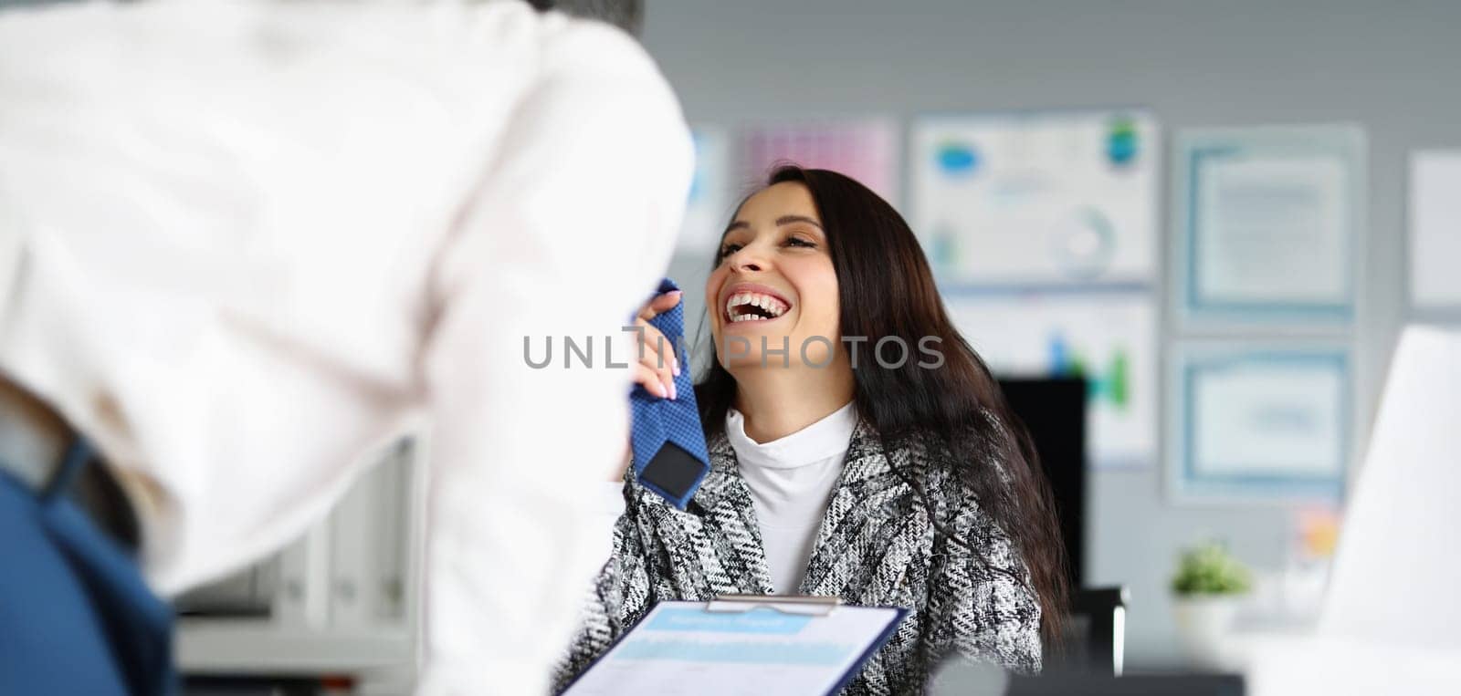 Portrait of businesswoman flirting with corporate male worker touching his tie and laughing. Female boss start relationship at work. Office romance concept