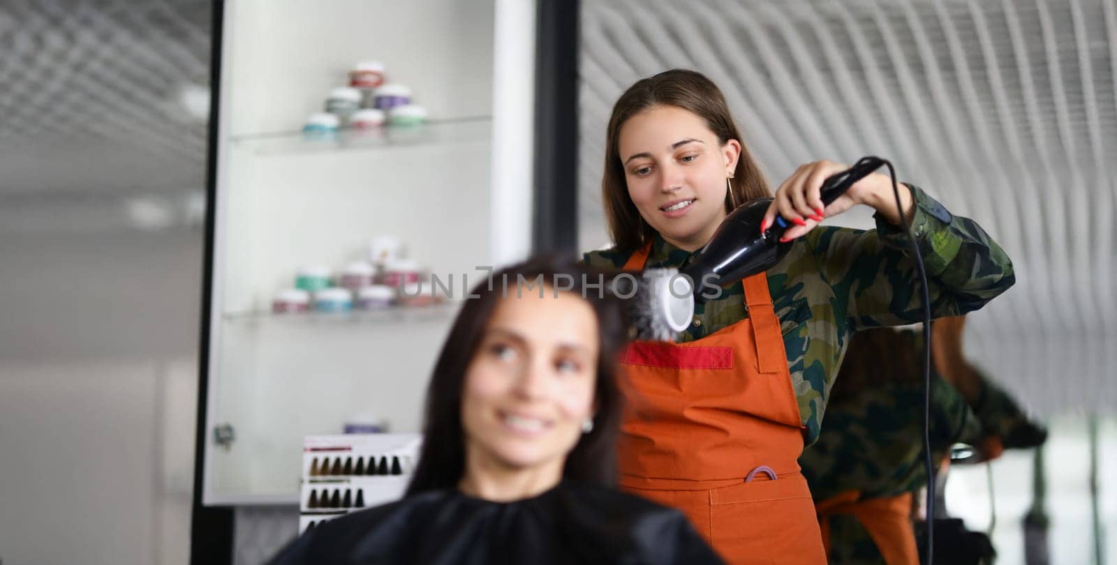 Portrait of smiling hairdresser using hairdryer for treatment with hair and being creative. Professional equipment for work with hair. Wellness concept