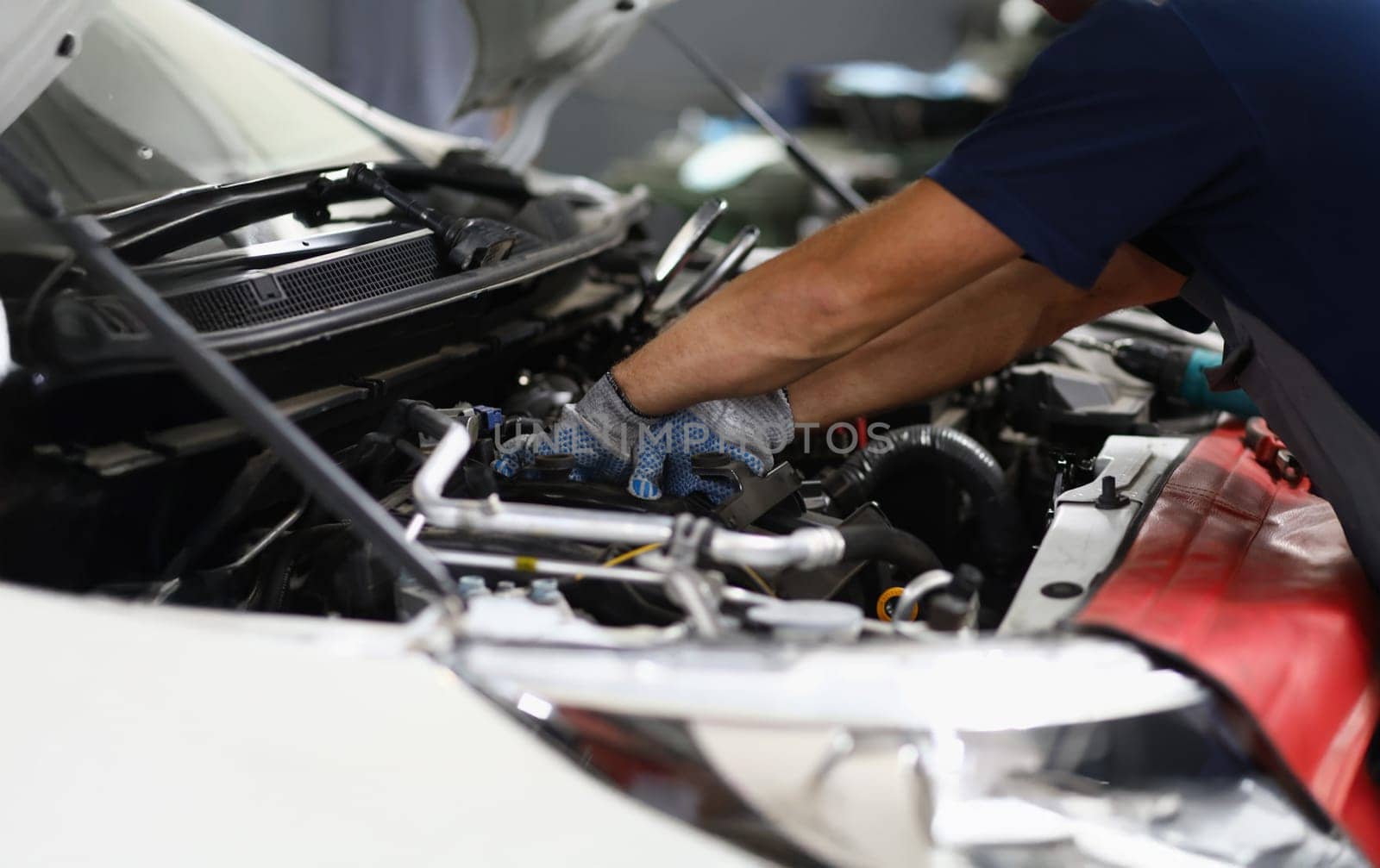 Close-up of professional mechanic male repair detail in automobile on pit station. Qualified garage worker in uniform fix car. Maintenance service concept