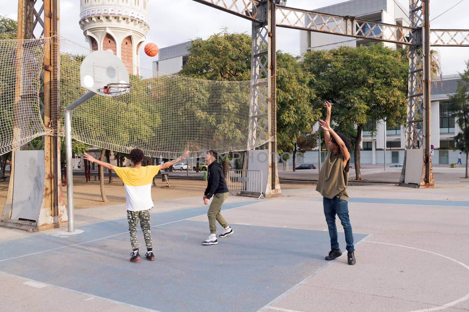 three focused multiethnic teen friends having fun playing basketball on sports ground in city park, concept of youth and urban lifestyle
