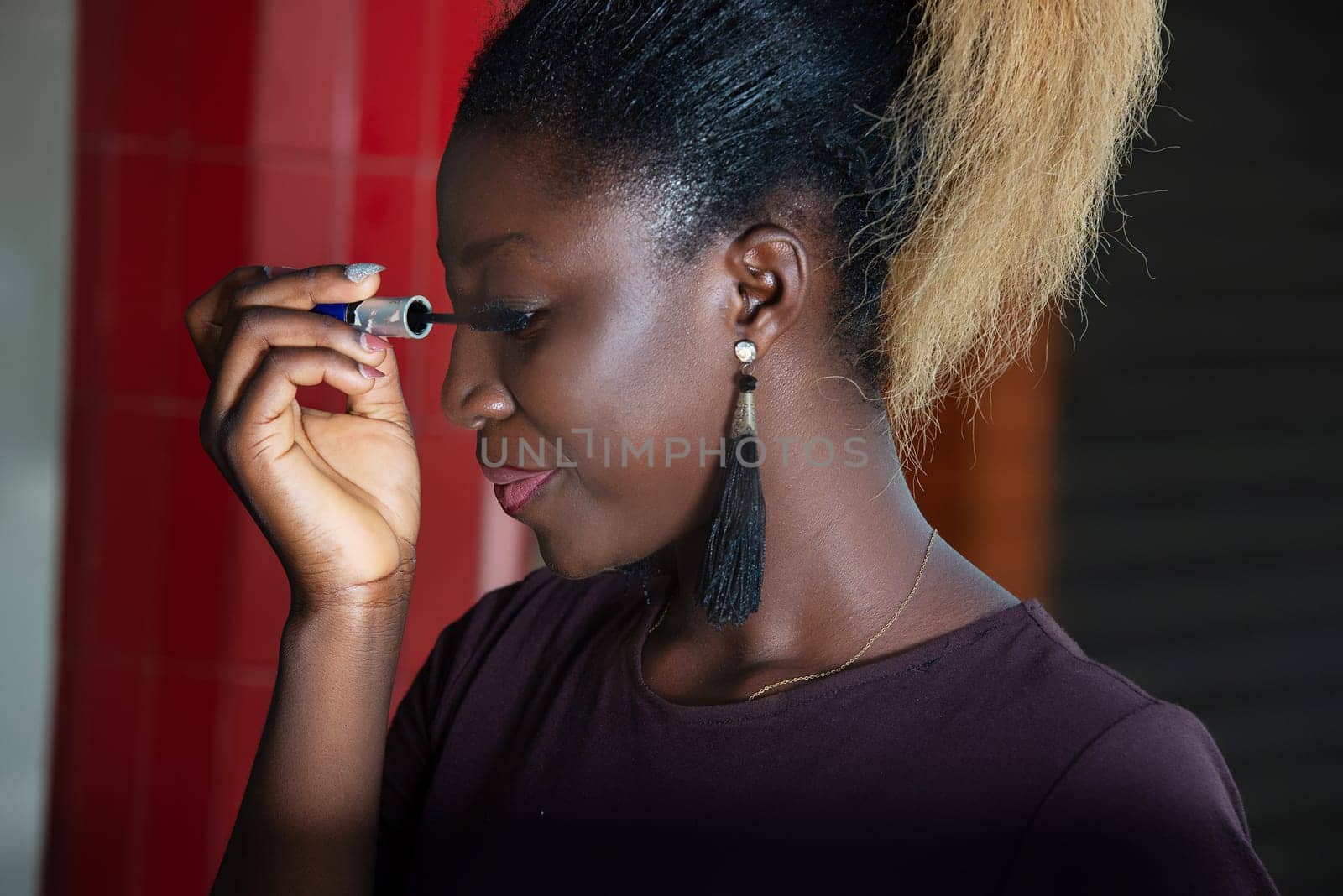 young girl standing in purple tee-shirt doing makeup while smiling.