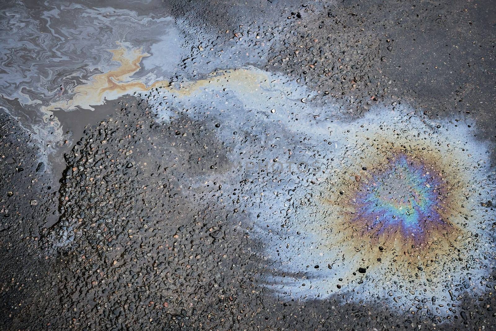 Close-up of shiny fuel spill on wet pavement on sunny fall day.