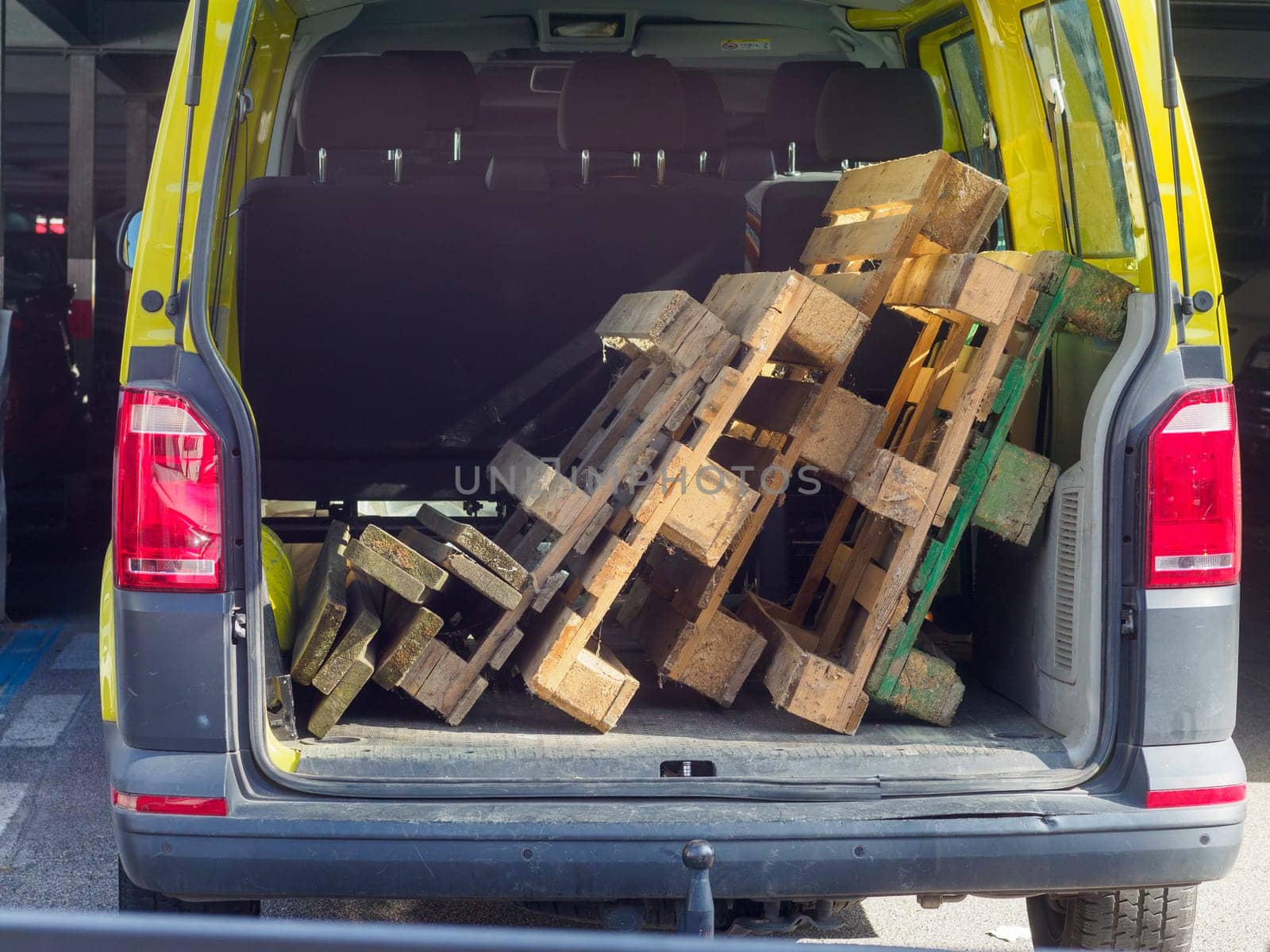 Yellow delivery van is parked with its back open, revealing a stack of wooden pallets taking up most of the cargo space. The van is prepared for transporting the pallets to their destination