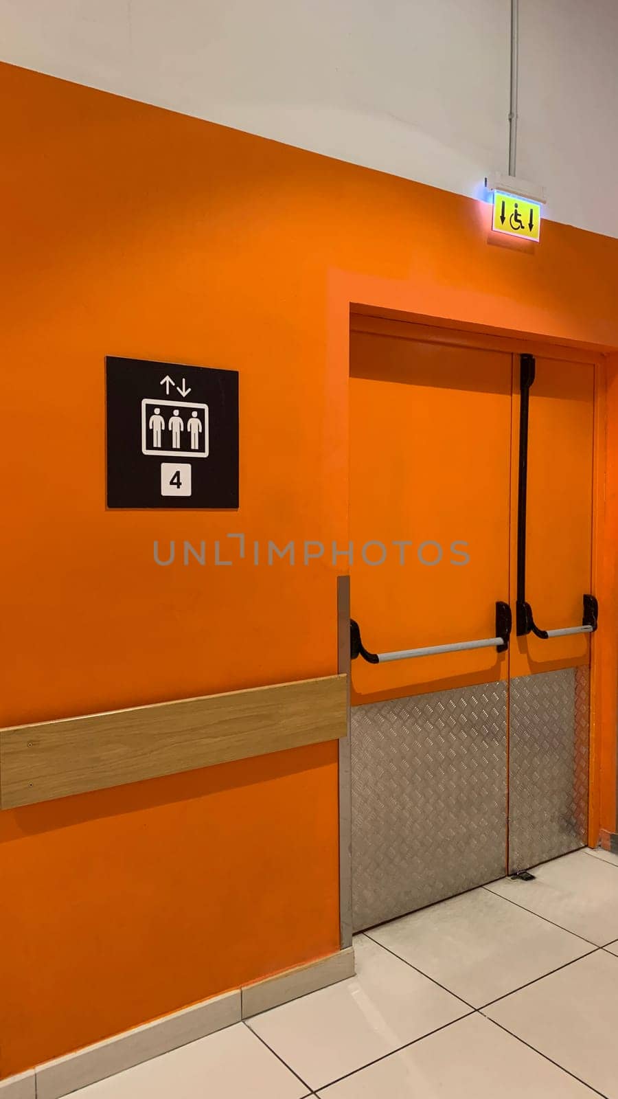 Entrance to service room with elevator in building with orange wall and sign indicating lift capacity is 4 people, sign with wheelchair above the entrance to special elevator