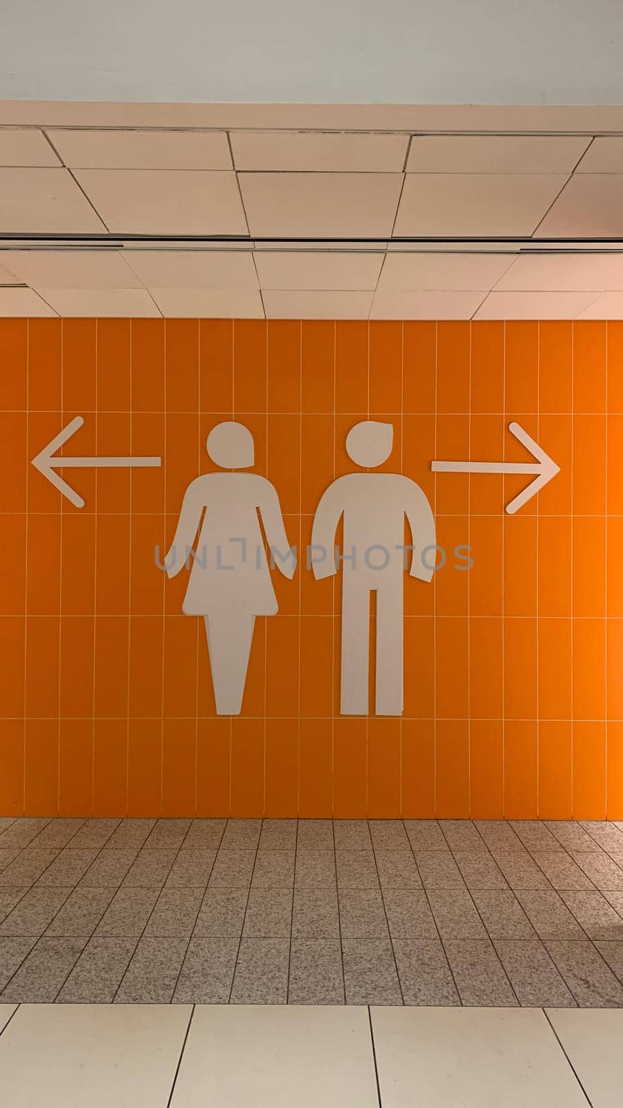 Wall with large male and female signs and directional arrows on orange wall at entrance to restroom. Direction to toilet with gender separation in restroom