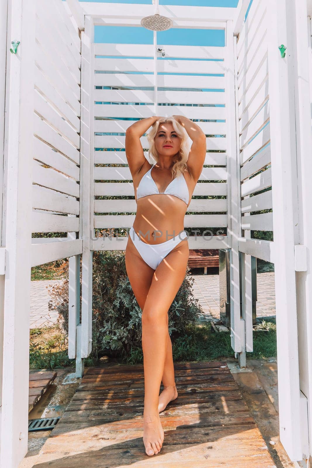 A woman in a bikini stands in front of a white shower stall. She is smiling and she is enjoying the moment.