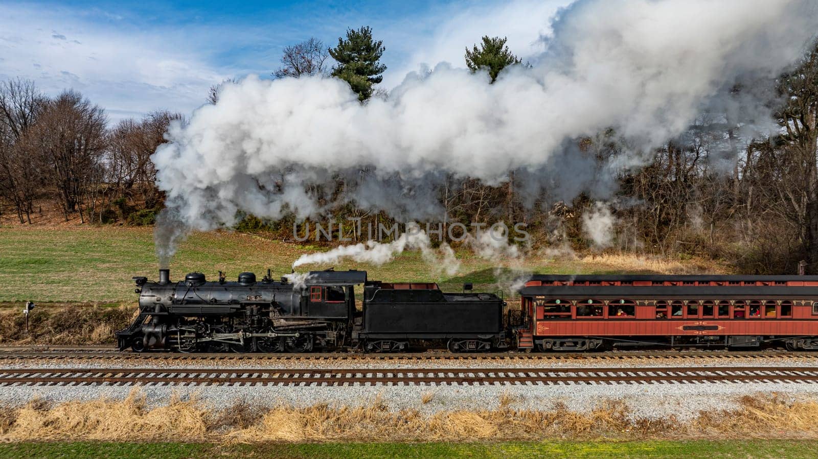 A classic steam locomotive billows smoke as it travels along the railway, framed by greenery and clear skies, showcasing the beauty of a bygone era in transportation.