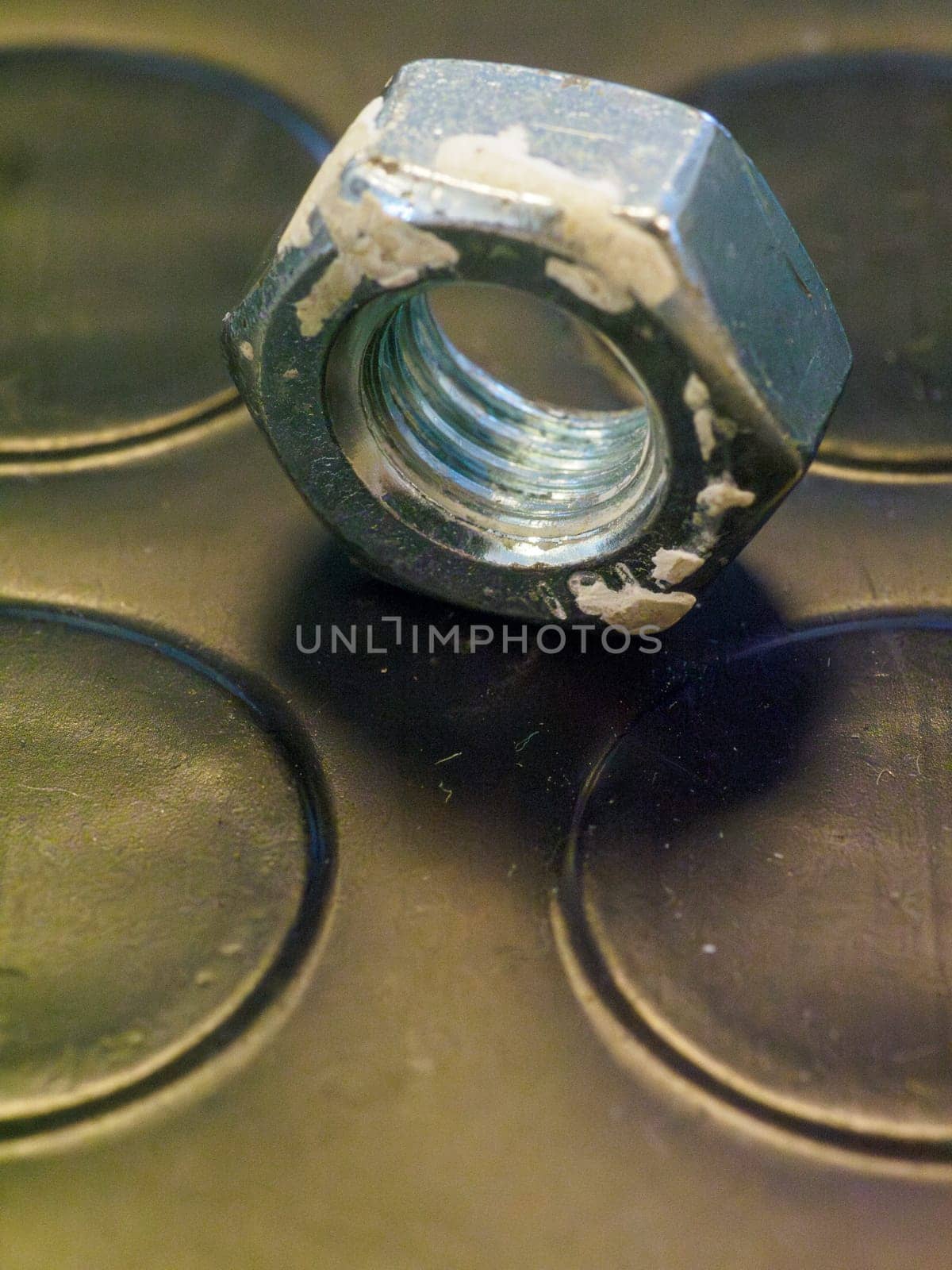 Worn metal nut, covered in construction dust, rests on a textured surface that boasts circular indentations, showcasing its industrial charm and mechanical strength