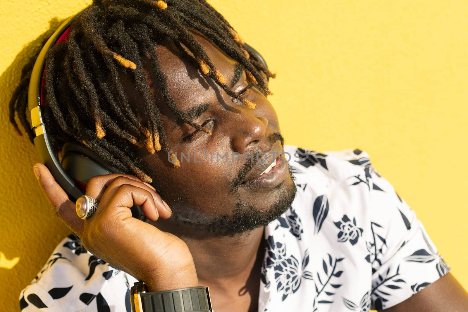 attractive young african man listening to and enjoying music with large headphones on yellow background, concept of technology and lifestyle, copy space for text