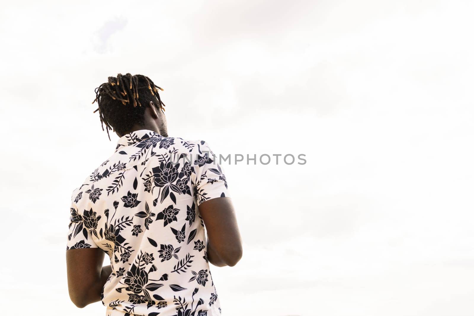 back view of a stylish young african american man in a flower shirt with the sky in the background, concept of freedom and lifestyle, copy space for text