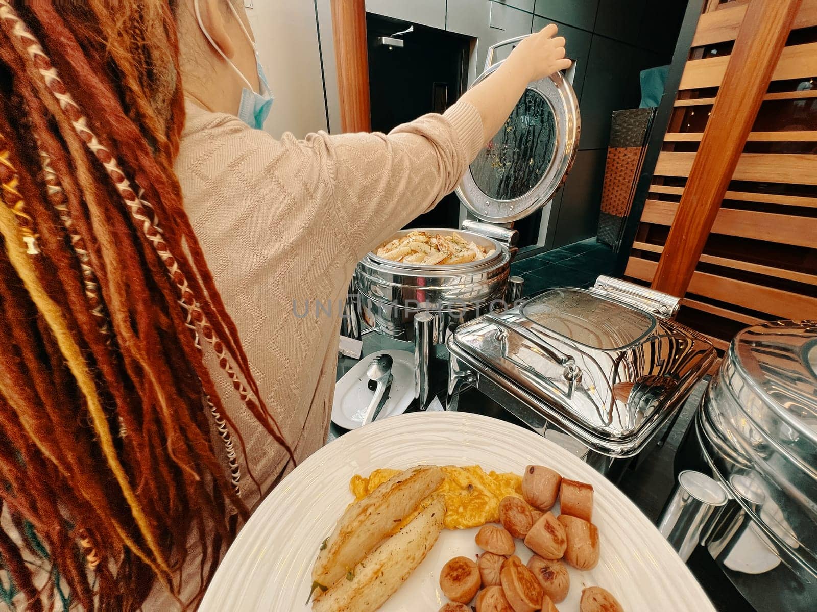 In a first-person perspective, a man is meticulously plating a dish. In a hotel, a woman is choosing food from a warming machine to fill up her plate at the buffet.