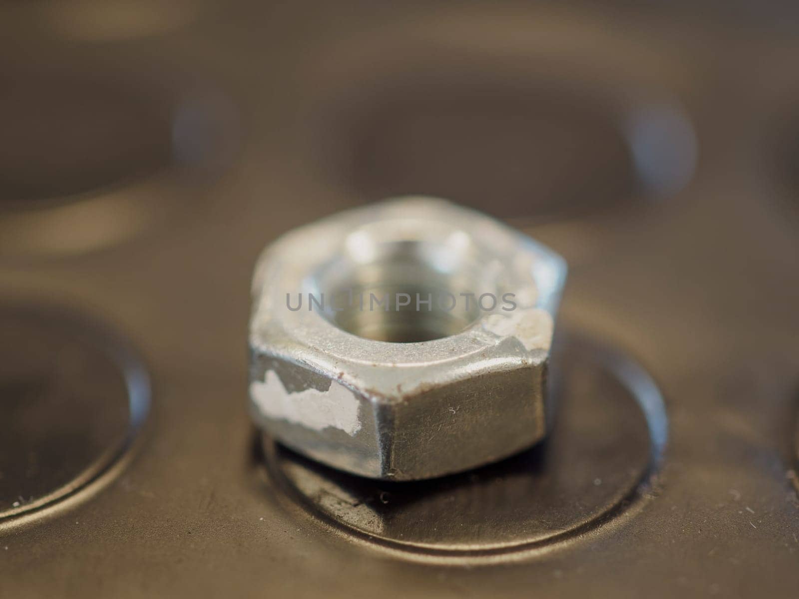 Chipped metal hex nut on a dark surface with circular indentations, showcasing industrial details. Close up highlights texture and shine, evoking engineering and manufacturing
