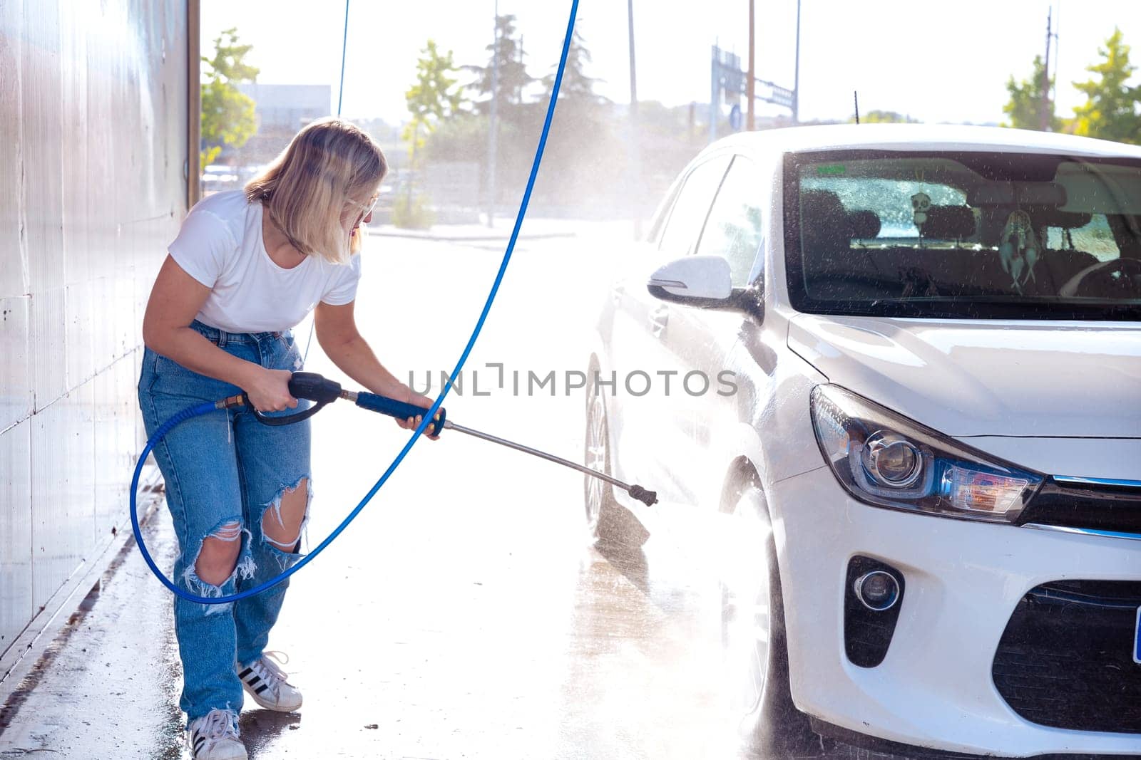 Image, portrait of a young, smiling, attractive woman washing a car in a car wash, car wash, foam cleaning, pressure water
