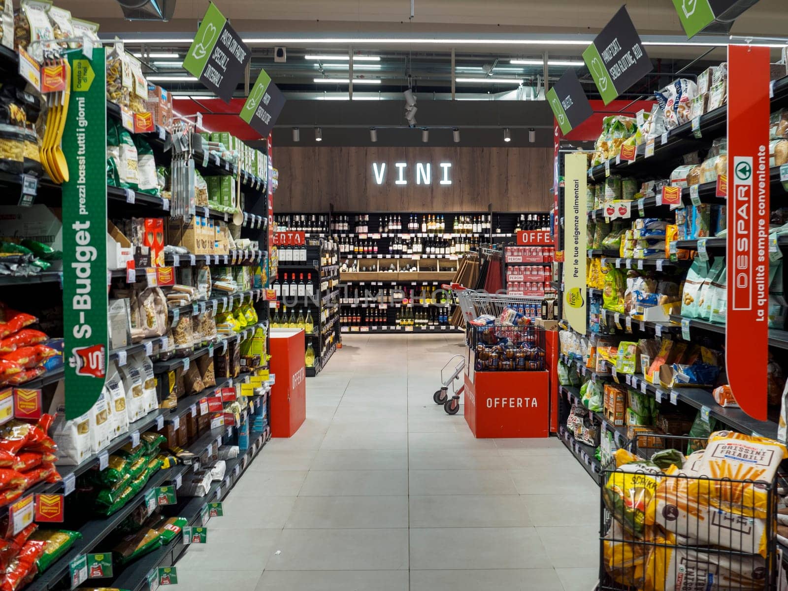 Cremona, Italy September 26th 2024 A modern supermarket aisle with a shopping cart standing between shelves full of various goods