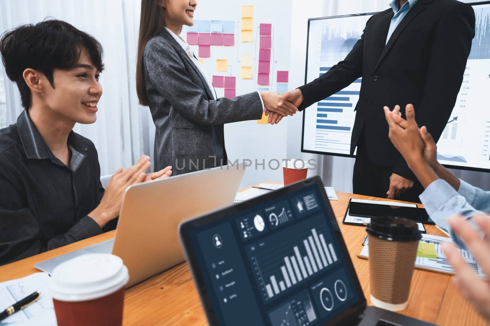 Diverse coworker celebrate with handshake and teamwork in corporate workplace. Happy business people united by handshaking after successful meeting or business presentation on data analysis. Concord