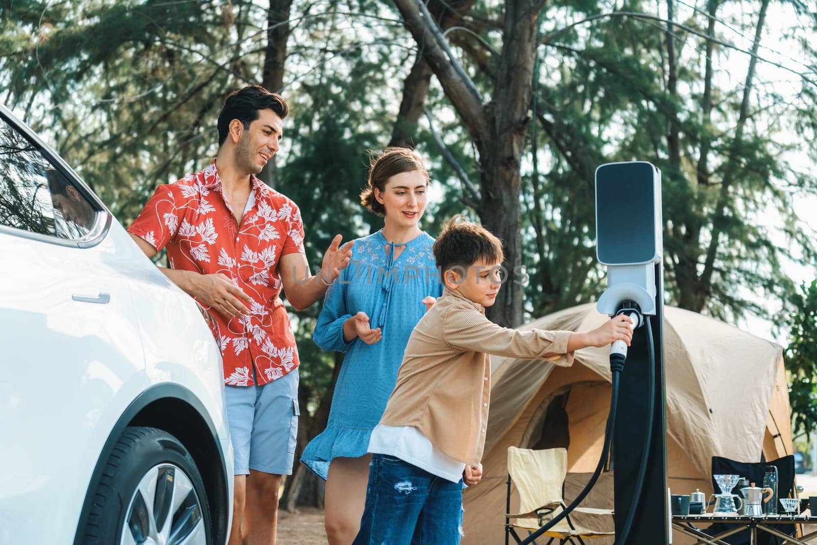 Outdoor adventure and family vacation camping in nature travel by eco friendly car for sustainable future. Lovely family recharge EV car with EV charging station in campsite. Perpetual