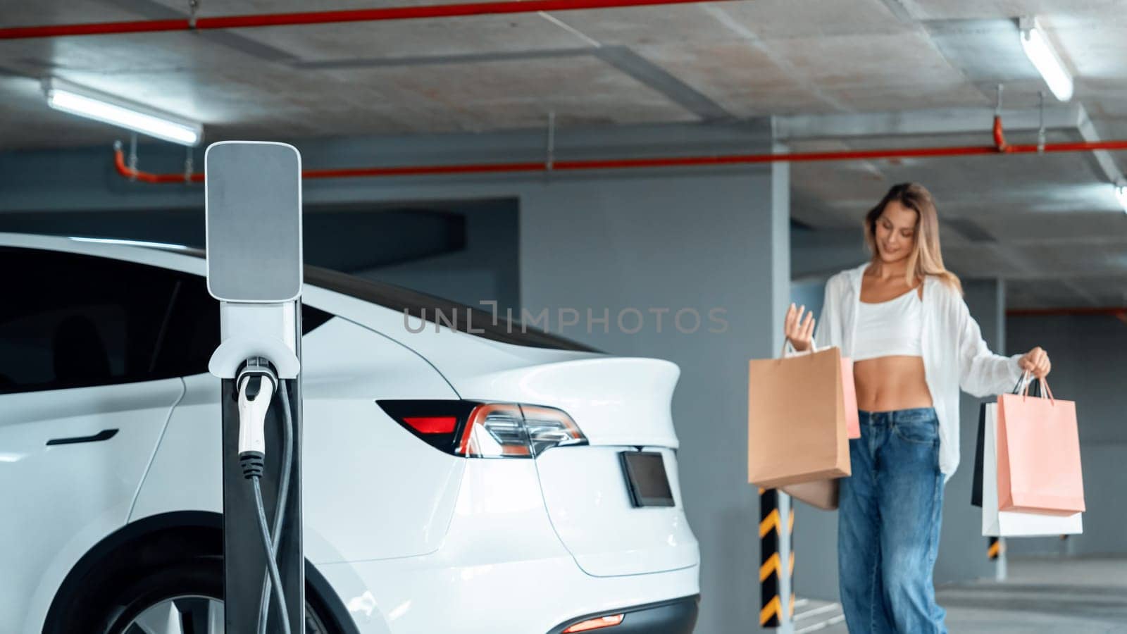 Young woman travel with EV electric car to shopping center parking lot charging in downtown city showing urban sustainability lifestyle by green clean rechargeable energy of electric vehicle innards