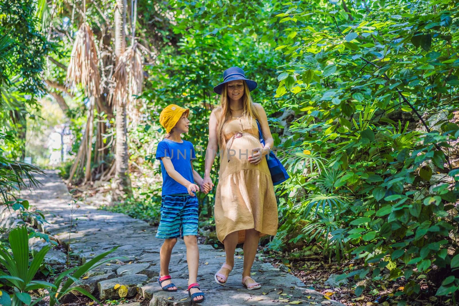 Expectant mother and her son enjoying a leisurely stroll in the park, cherishing precious moments amidst nature's beauty.