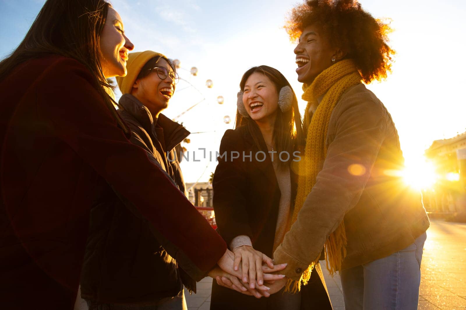 Group of multiracial college students stack hands together in a circle as symbol of community and friendship outdoors on a winter day. Community and cooperation concepts.