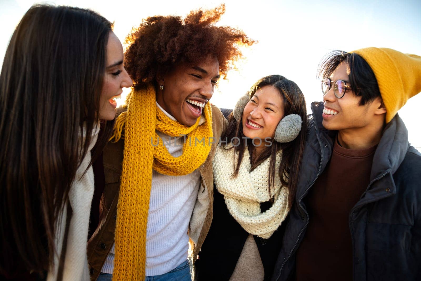 Multiethnic college student friends enjoying sunny winter day together. Young happy people embracing having fun outdoors talking and laughing.Lifestyle concept.